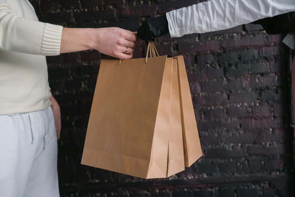 Two individuals exchange paper shopping bags against a dark brick wall background.