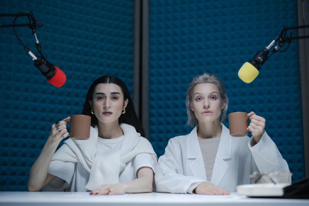 Two women hosting a podcast in a studio with microphones and coffee mugs.